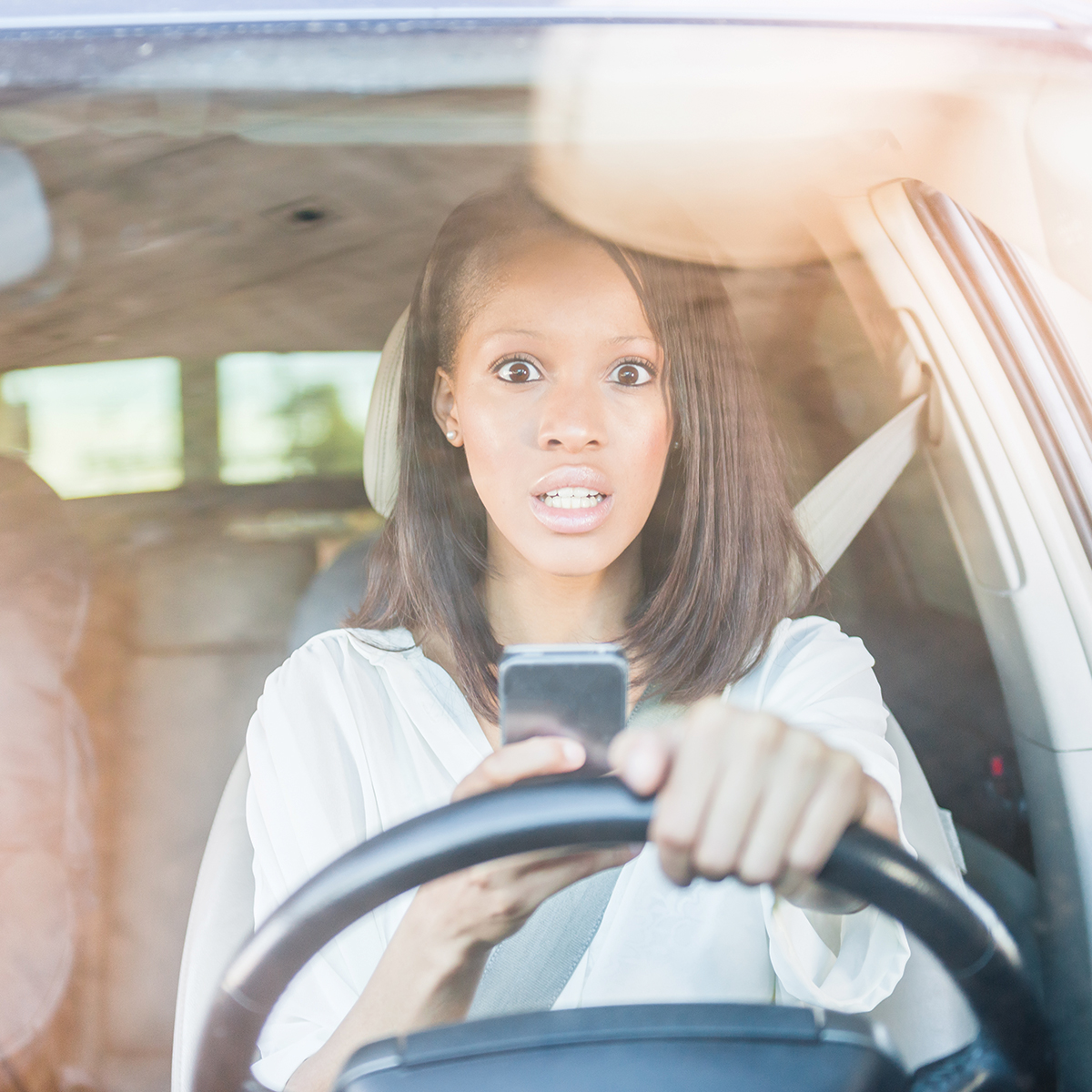 Teen driving while look at her cell phone and being distracted 