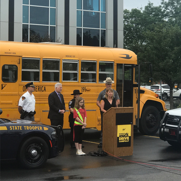 Press conference at AAA in front of a school bus with police, student and Director of Public Relations to promote student safety