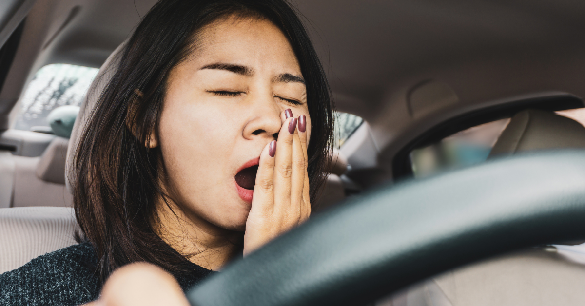 Tired woman sitting behind the wheel and yawning.