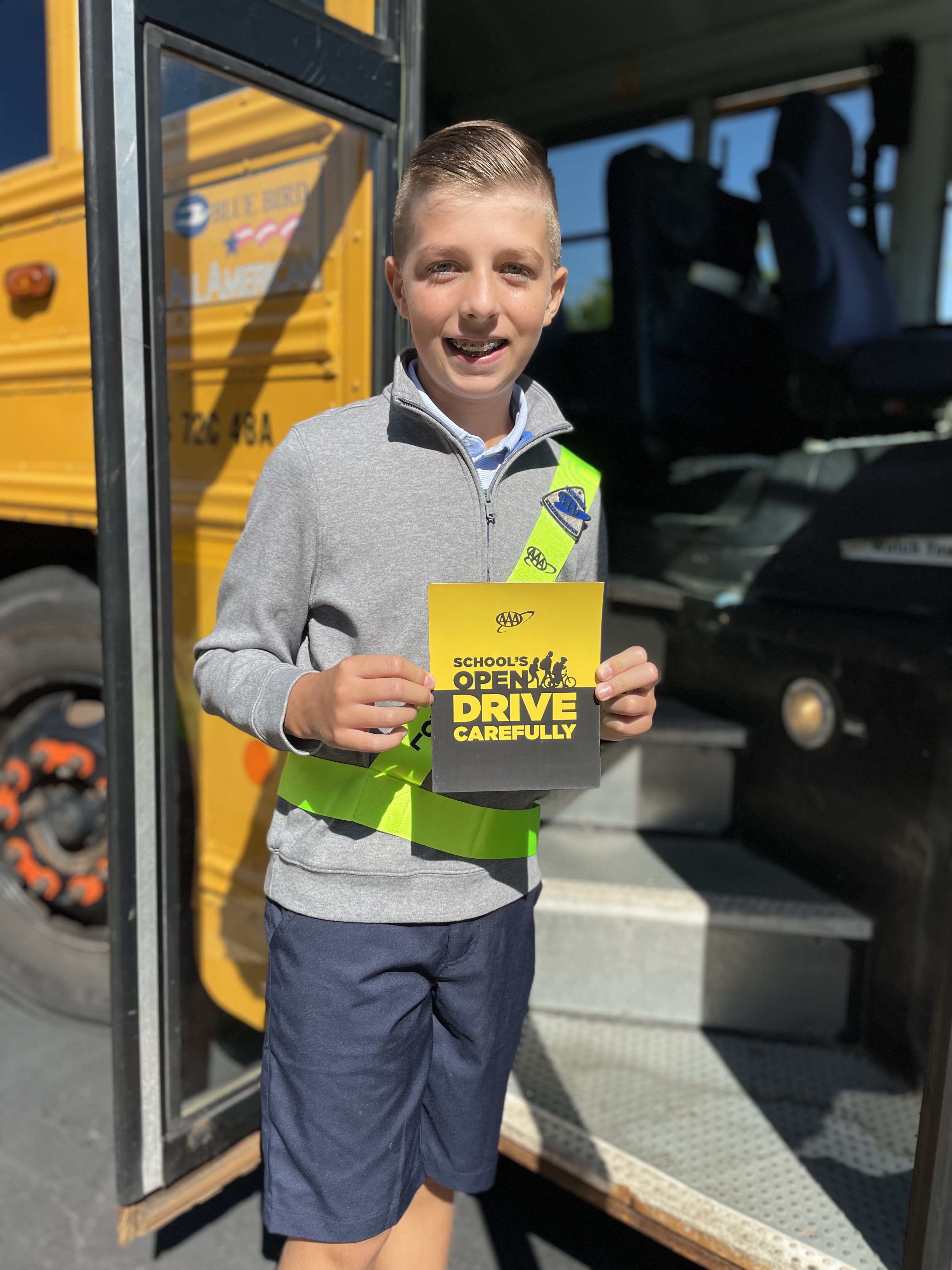AAA School Safety Patroller  boards a school bus and poses with a School's Open, Drive Carefully magnet