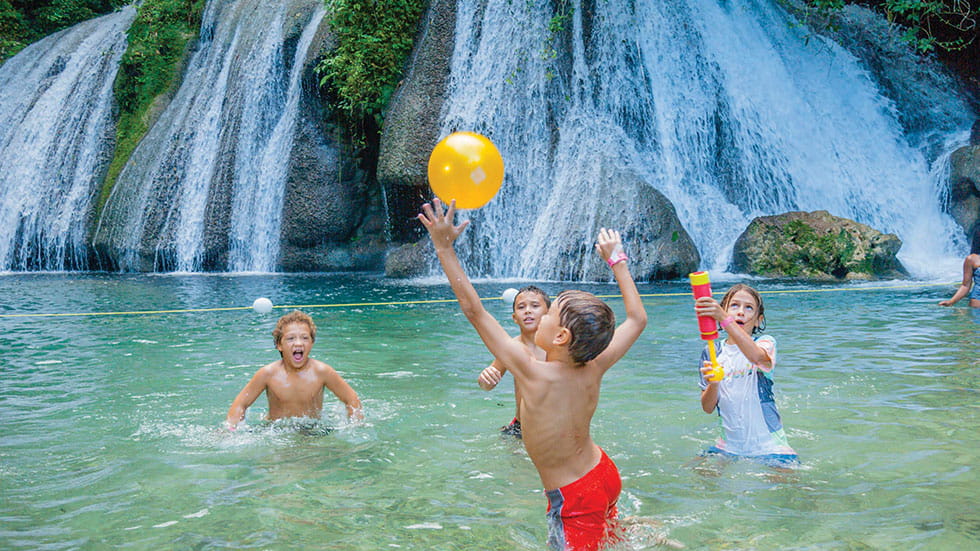 Kids playing in water in a lagoon alonside a waterfall
