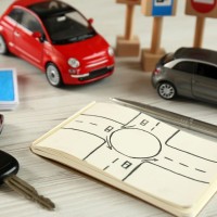 Toy cars are used as representation in driver training, with a notepad nearby with a drawing of a four-way stop.
